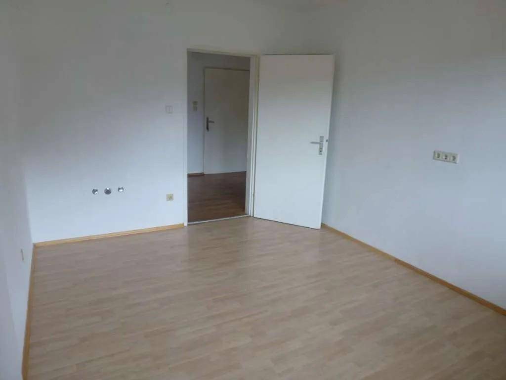 Helles Zimmer mit hellem Laminatboden und offener Tür zu einem weiteren Raum.
