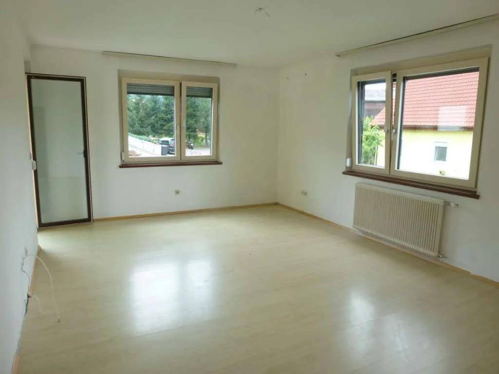 Helles, leeres Zimmer mit großen Fenstern und hellem Laminatboden.