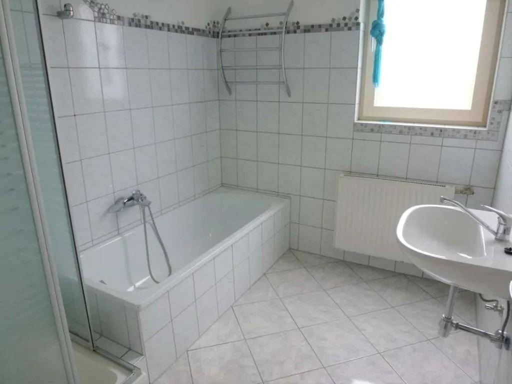 Badezimmer mit Badewanne, Waschbecken, Fliesenboden und Fenster.