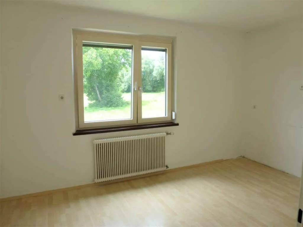 Helles Zimmer mit Fenster und Blick ins Grüne, ausgestattet mit hellem Laminatboden.