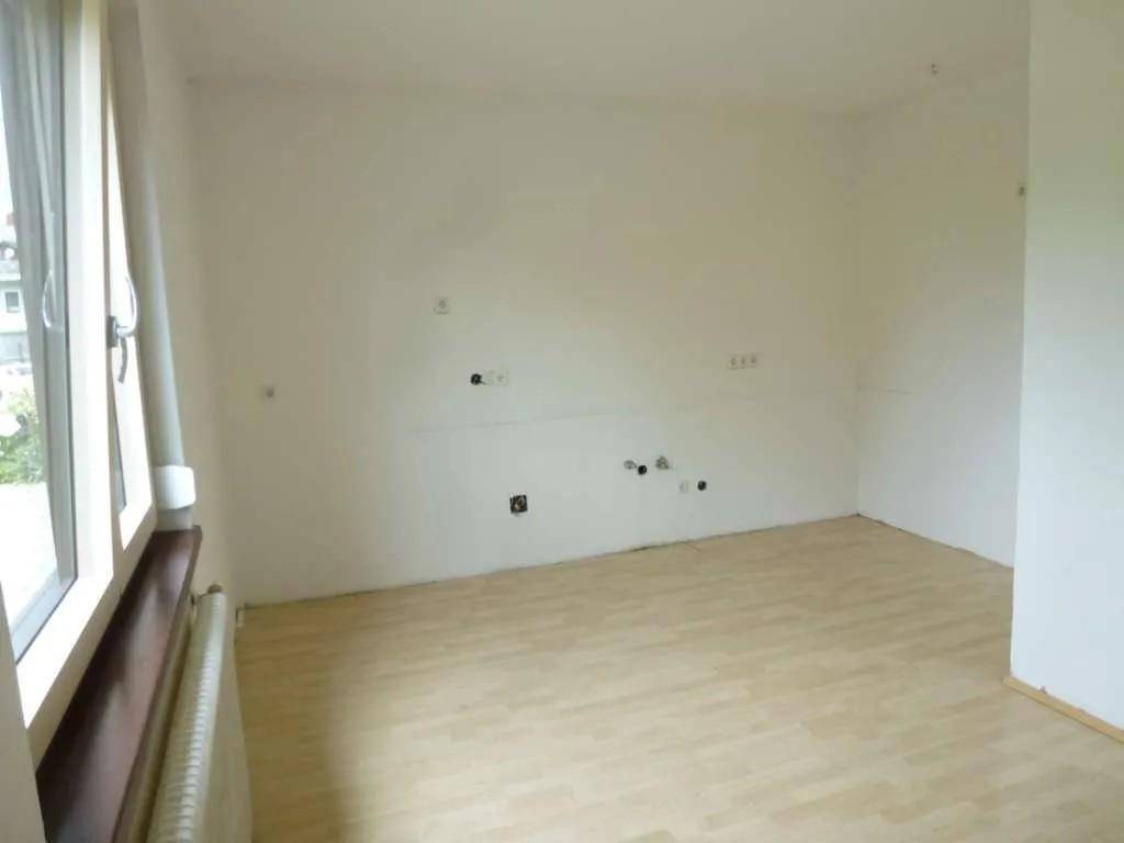 Leerer Raum mit Anschlüssen für eine Küche und hellem Laminatboden.
