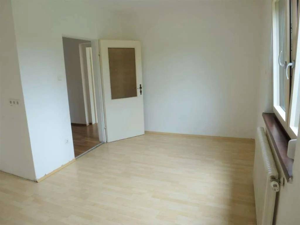Helles Zimmer mit hellem Laminatboden und einer Tür zu einem weiteren Raum.