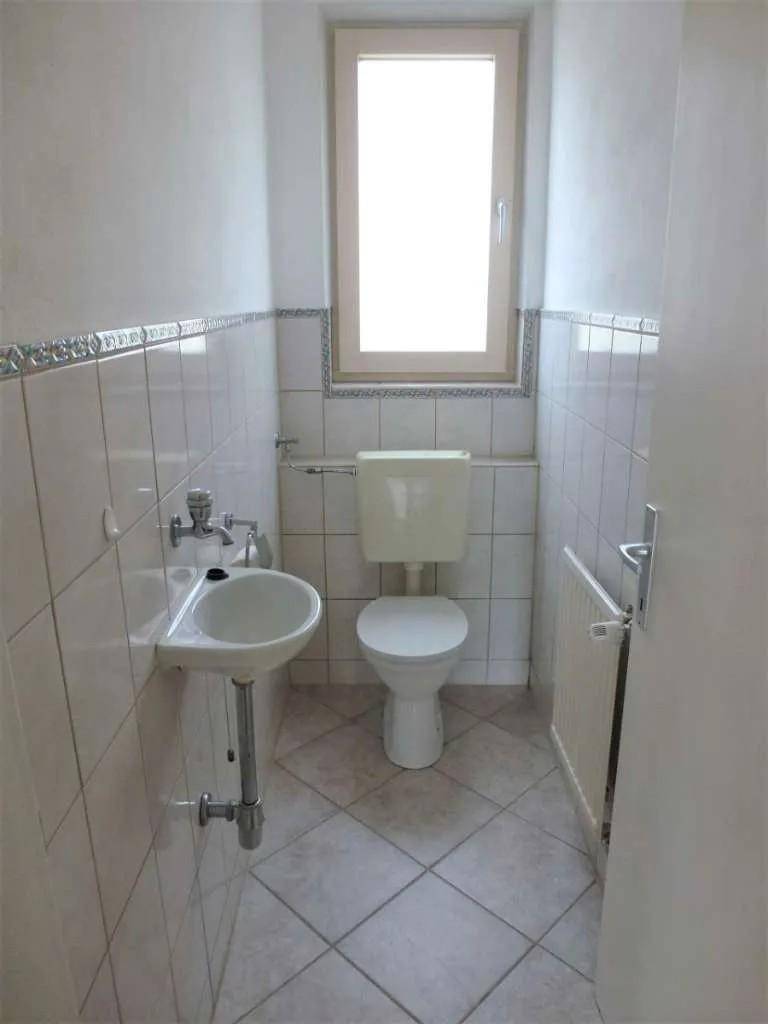 Kleines Gäste-WC mit Fenster, Fliesenboden und einfacher Ausstattung.