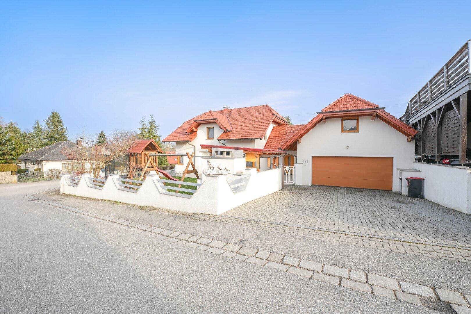 Ansicht des Einfamilienhauses von der Straße mit gepflasterter Einfahrt und Spielplatz im Vorgarten.