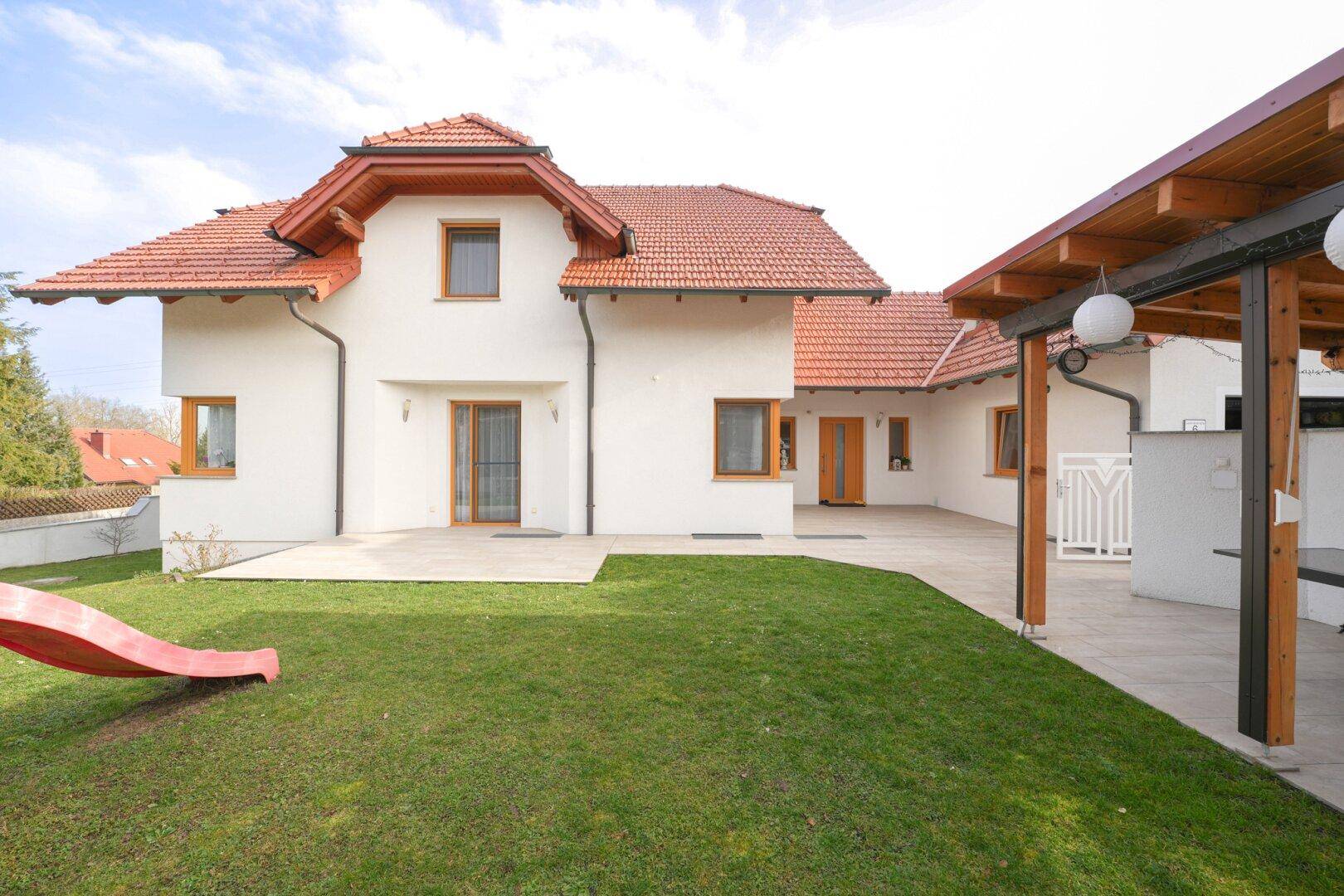 Rückansicht des Hauses mit gepflegtem Rasen, Terrasse und einer Kinderrutsche im Garten.