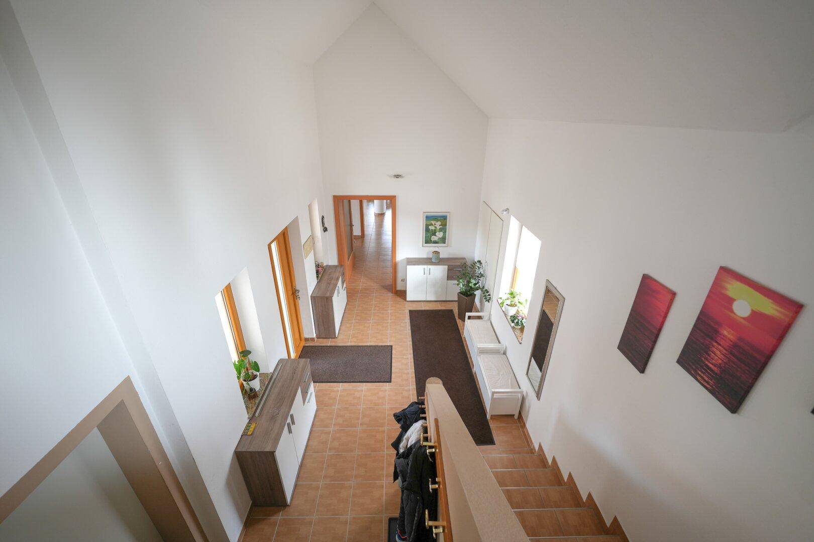 Geräumiger Eingangsbereich mit Fliesenboden, hohen Decken und Treppenaufgang.