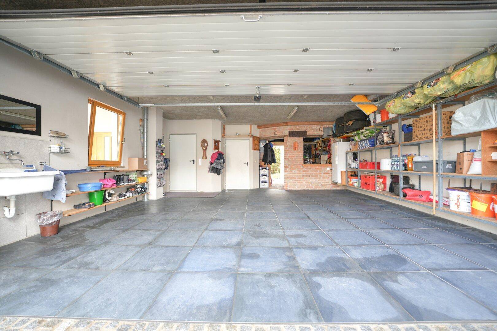 Geräumige Garage mit Fliesenboden, Waschbecken und praktischem Stauraum.