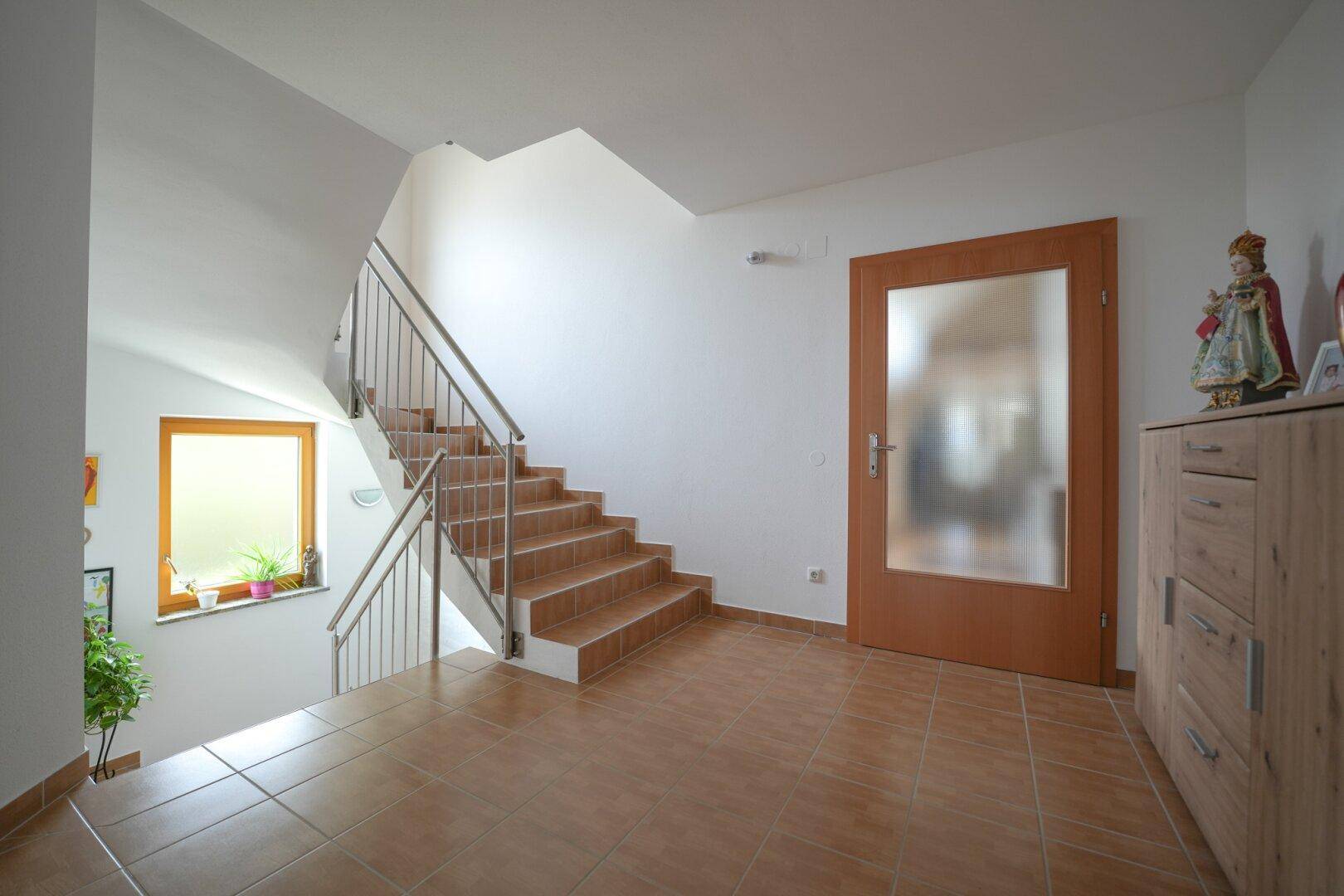 Helles Treppenhaus mit Fliesenboden, Holzfenster und Zugang zu den oberen Etagen.