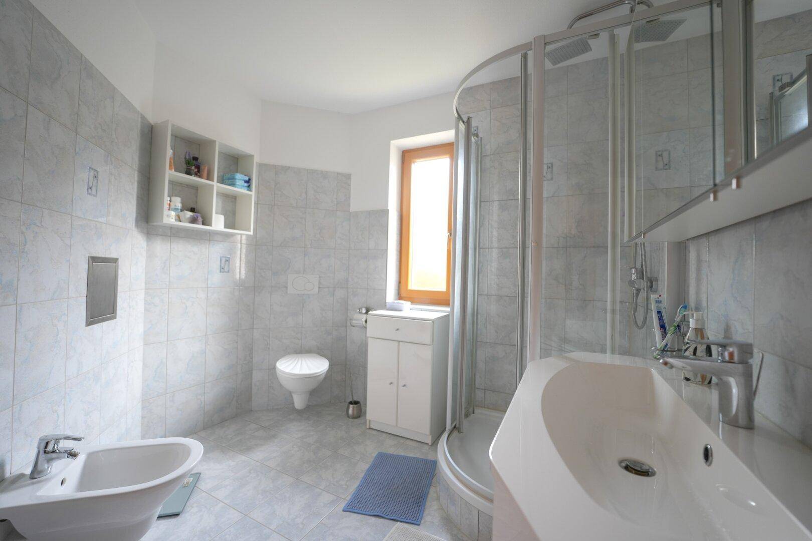 Modernes Badezimmer mit Dusche, WC, Bidet und Fenster für natürliche Belüftung.