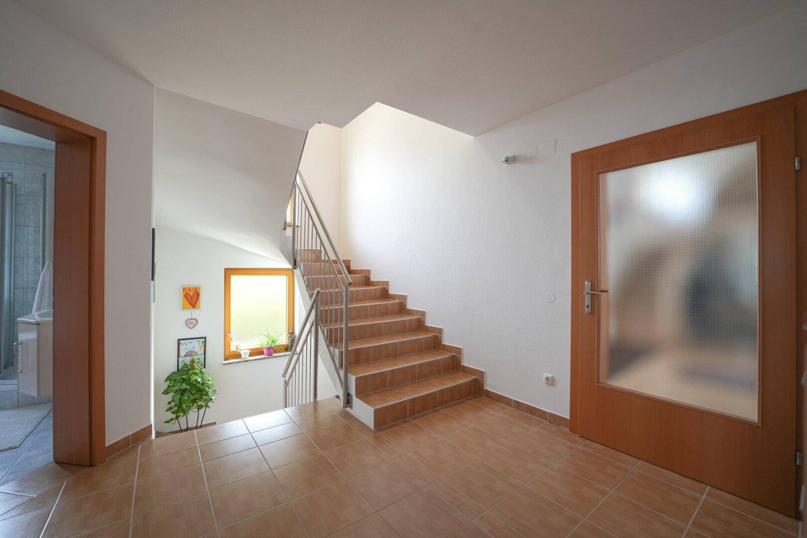 Helles Treppenhaus mit Fliesenboden, Holzfenster und Zugang zu den oberen Etagen.