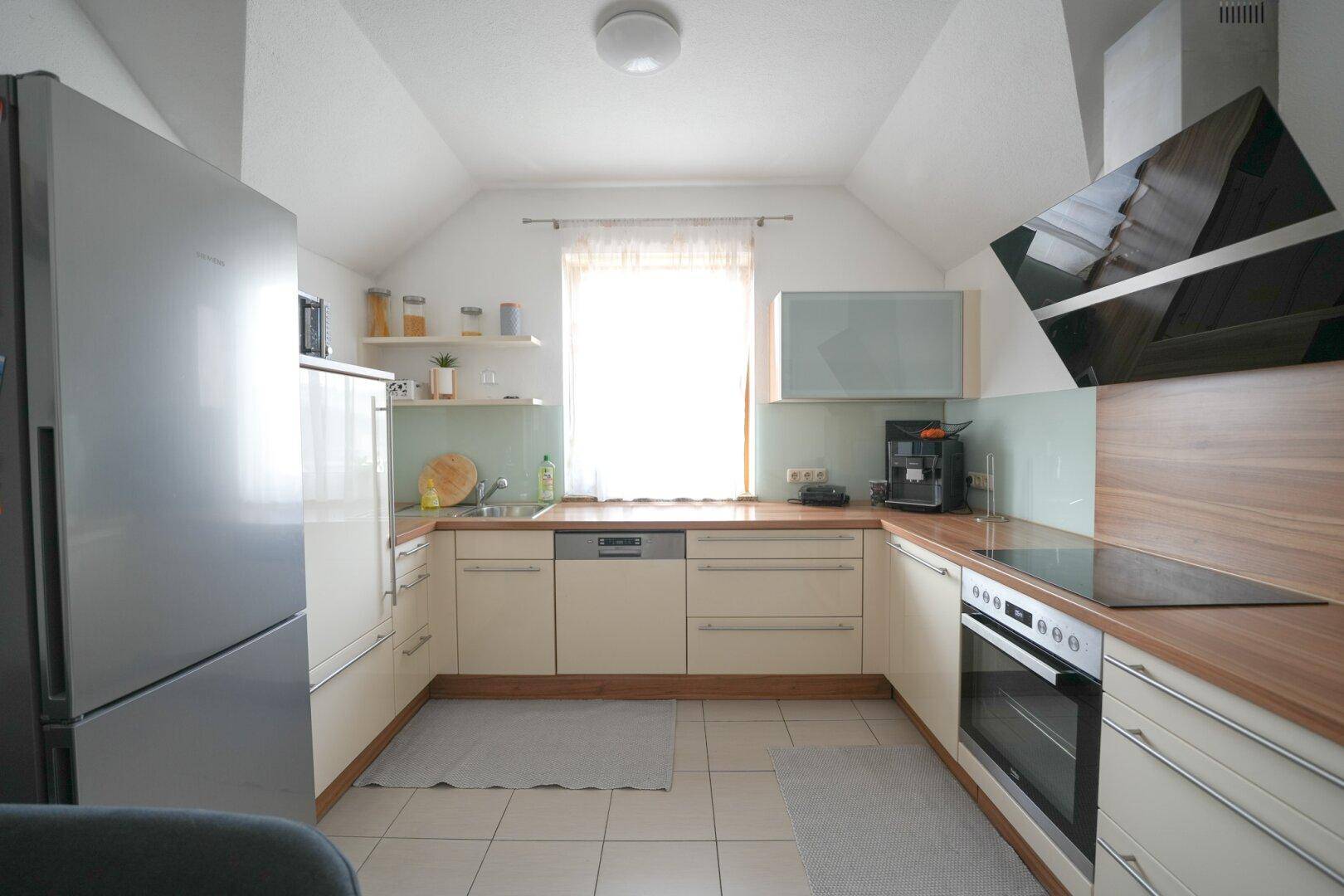 Moderne Einbauküche im Dachgeschoss mit Induktionskochfeld, Backofen und Holz-Arbeitsplatte.