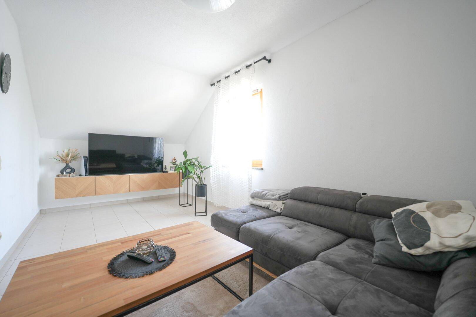 Gemütlicher Wohnbereich im Dachgeschoss mit Sofa, Holztisch und viel Tageslicht.