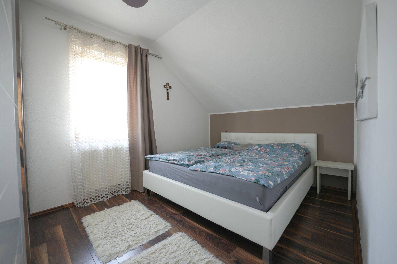 Schlafzimmer im Dachgeschoss mit Doppelbett, dunklem Holzboden und Dachschräge.