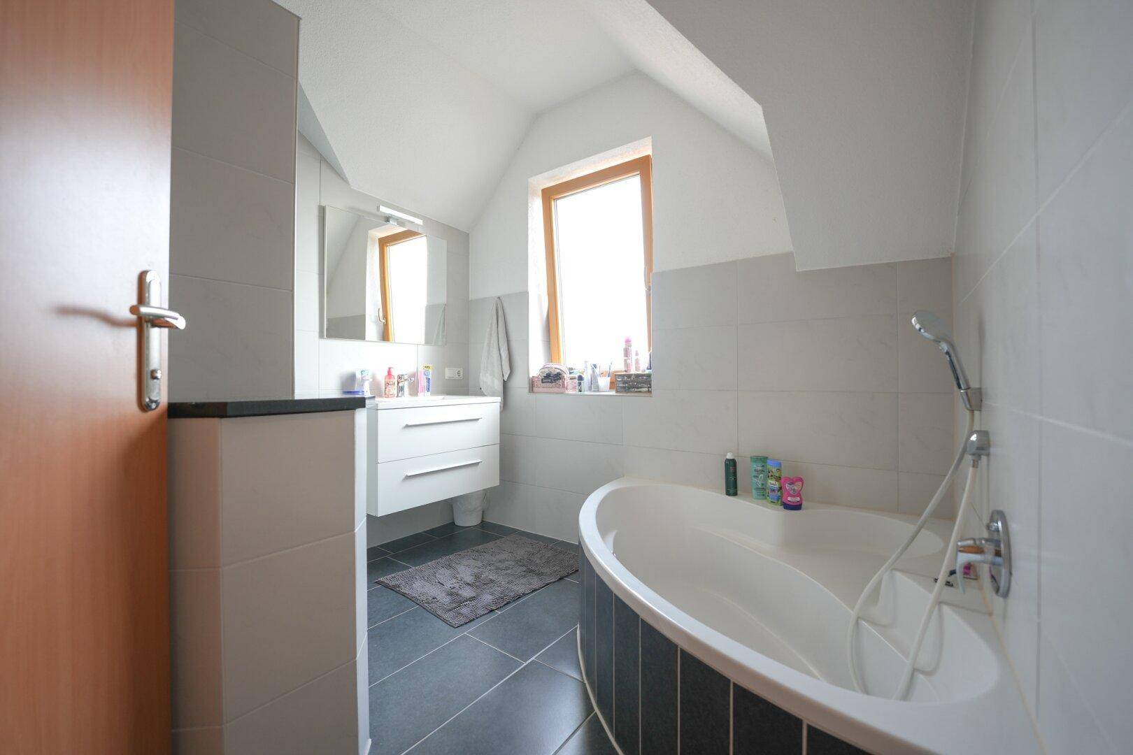 Modernes Badezimmer im Dachgeschoss mit Badewanne, Waschtisch und Fenster.