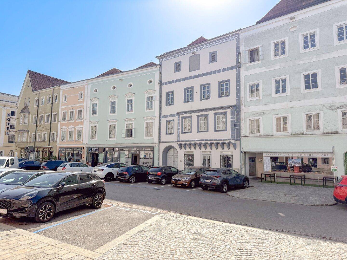 Panoramablick auf eine historische Häuserzeile mit geparkten Fahrzeugen und klarem Himmel.