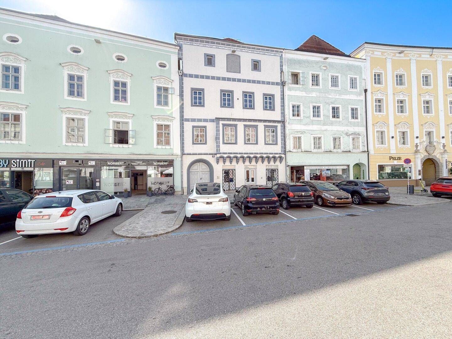 Straßenansicht einer Reihe farbenfroher historischer Gebäude mit geparkten Autos an einem sonnigen Tag.