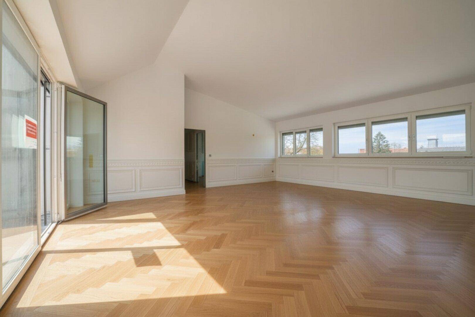 Weitläufiger, lichtdurchfluteter Wohnbereich mit Fischgrätparkett und breiten Fensterfronten.