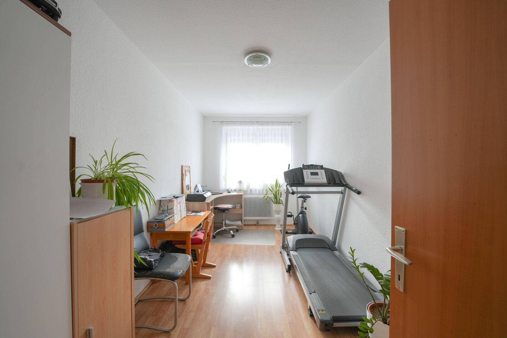 Helles Zimmer, ideal als Büro oder Fitnessraum, mit Fenster und Holzboden.