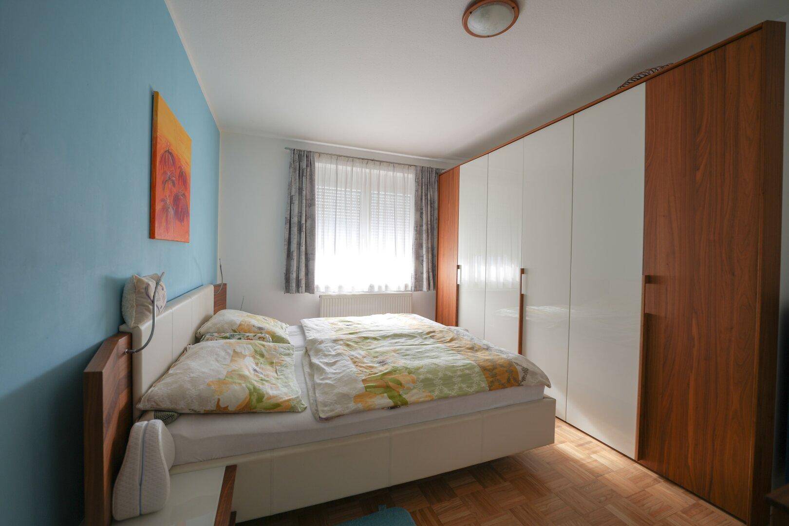 Schlafzimmer mit Doppelbett, großem Kleiderschrank und blauer Akzentwand.
