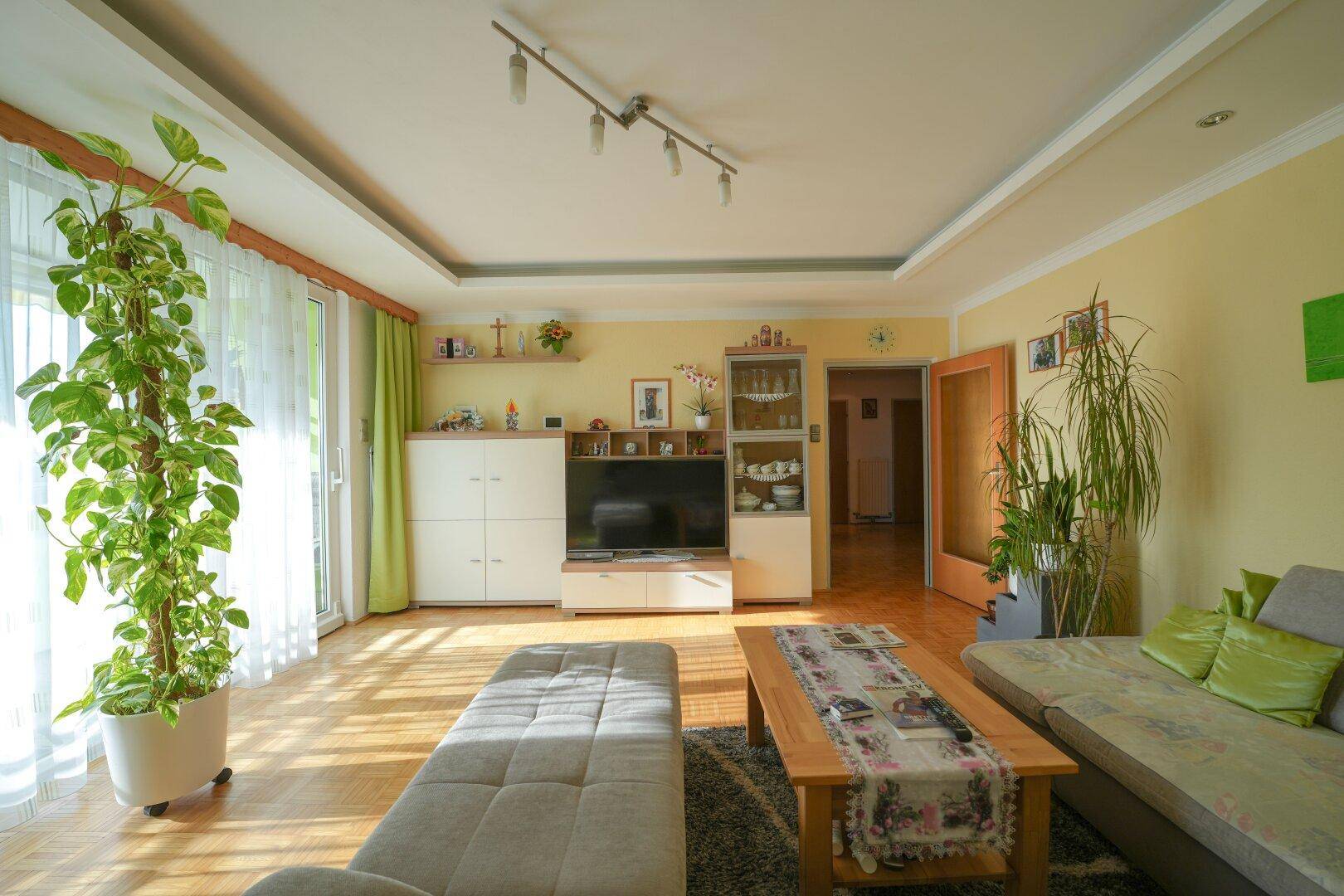 Helles Wohnzimmer mit Parkettboden, großen Fenstern und gemütlicher Sitzecke.