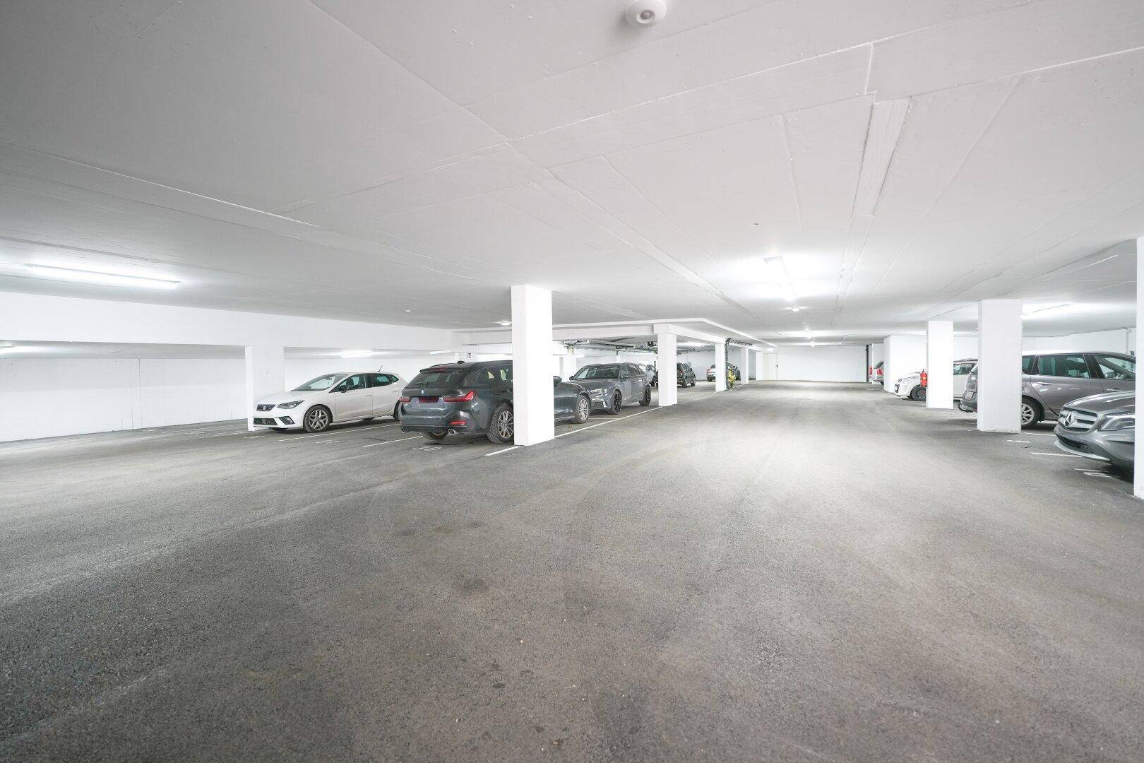 Geräumige Tiefgarage mit zahlreichen geparkten Fahrzeugen und heller Deckenbeleuchtung.