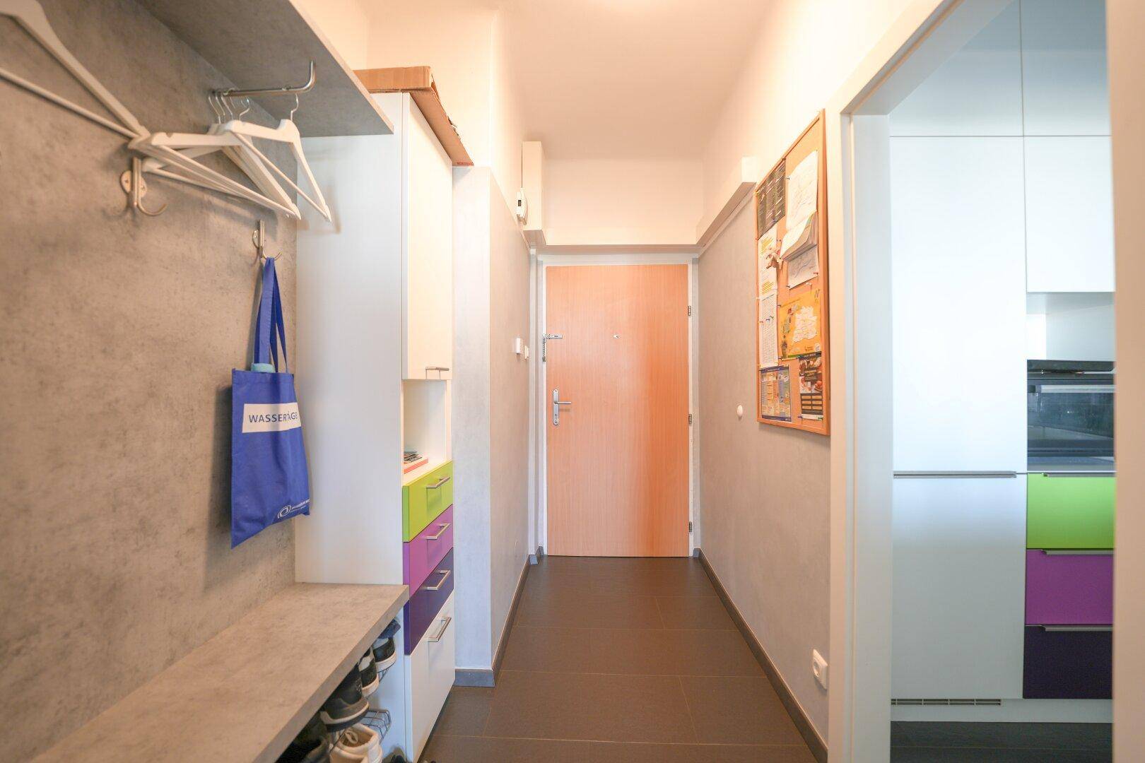 Eingangsbereich mit praktischen Einbauschränken, farbigen Schubladen und dunklem Fliesenboden.