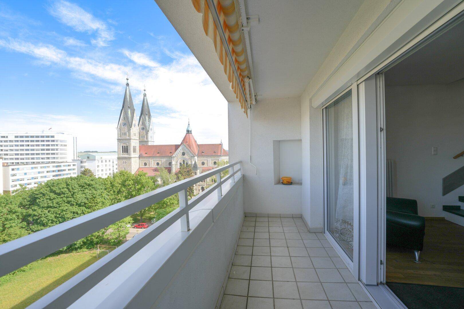 Balkon mit Blick auf eine historische Kirche, grüne Bäume und die Stadt, mit Zugang zum Innenbereich.