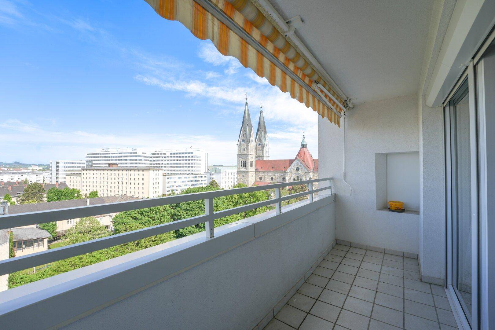 Balkon mit Panoramablick auf die Stadt, grüne Flächen und eine beeindruckende Kirche.