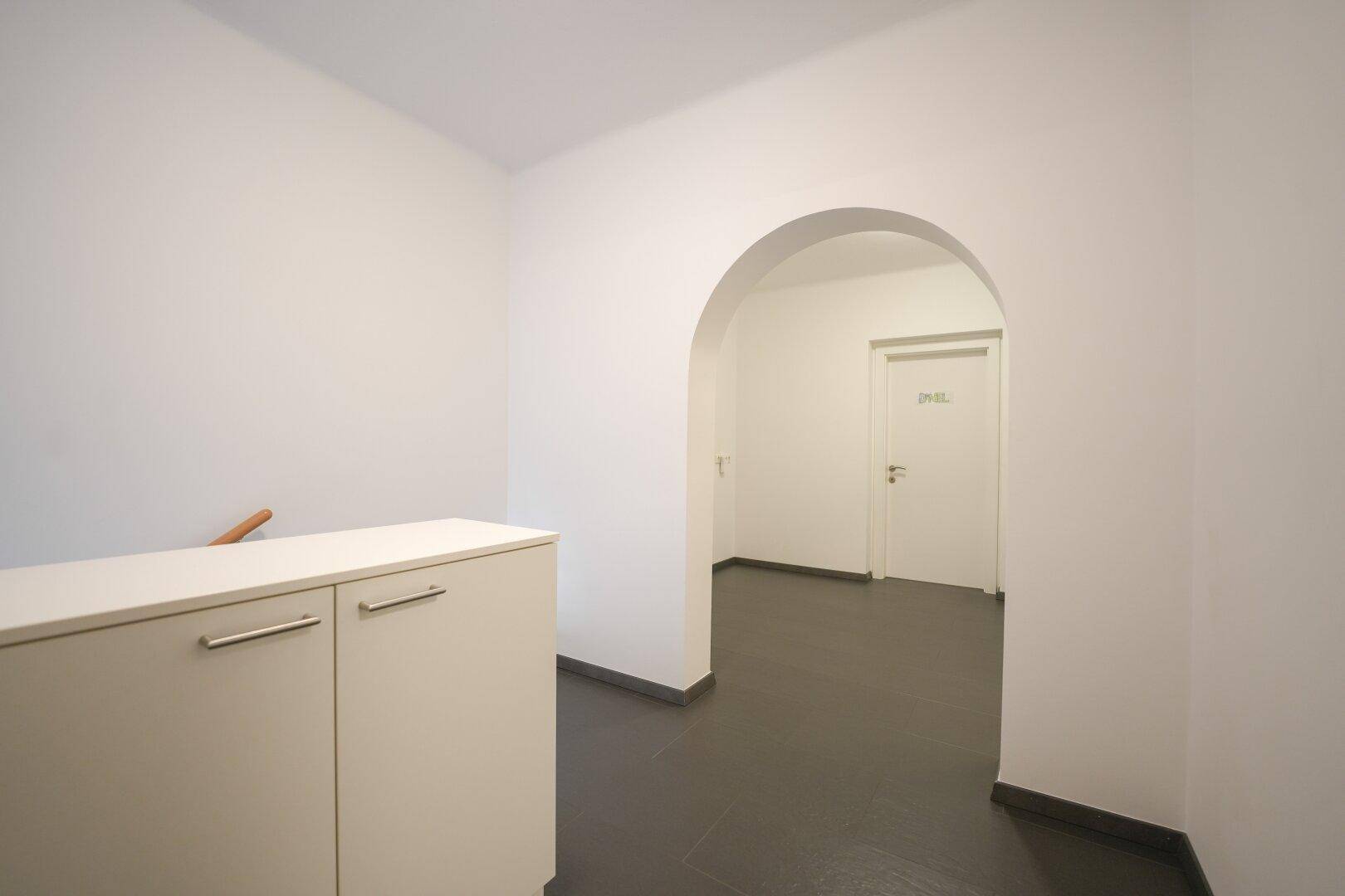 Heller Flur mit weiß gestrichenen Wänden, dunklem Fliesenboden und einem eleganten Torbogen.