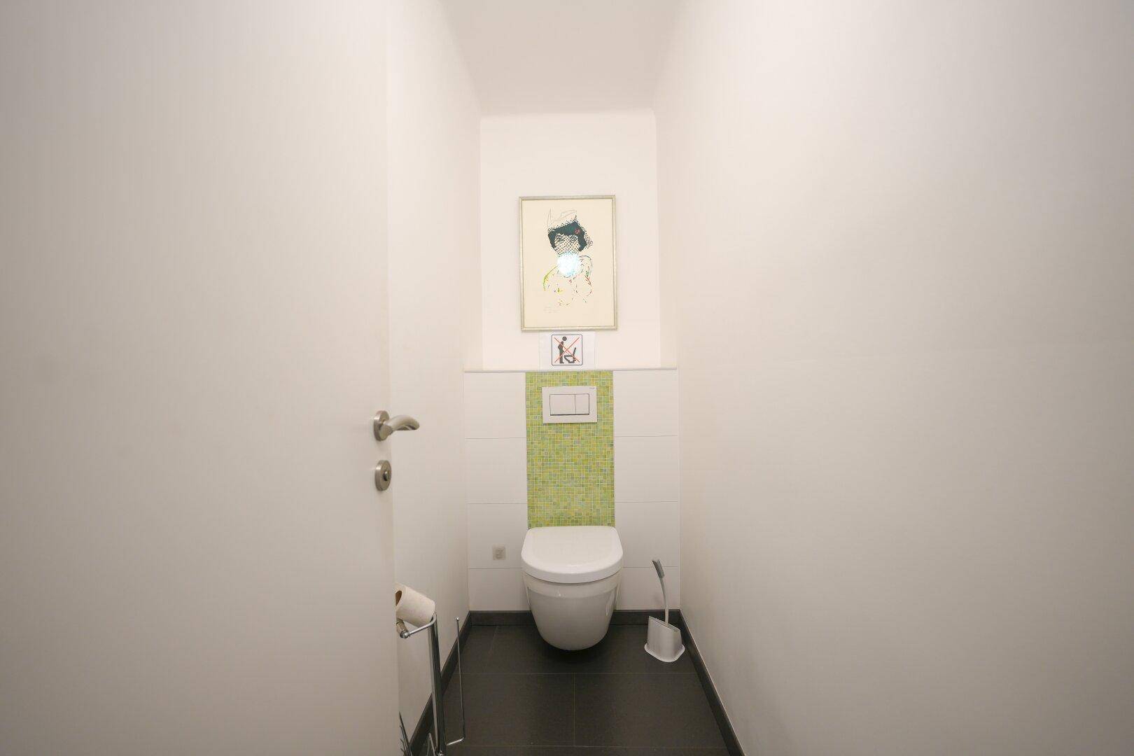 Separates Gäste-WC mit wandhängender Toilette und einer grünen Akzentwand aus Fliesen.
