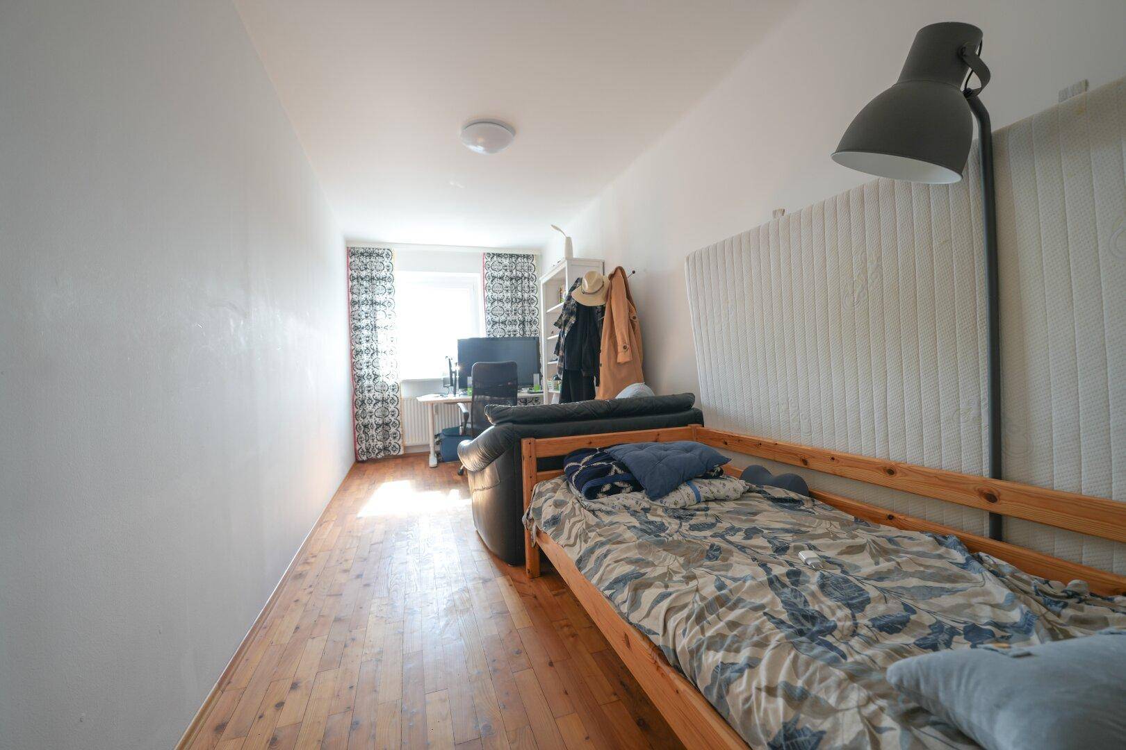 Helles Schlafzimmer mit Einzelbett, Schreibtisch, Sofa und Holzboden, ideal für Studenten oder Gäste.