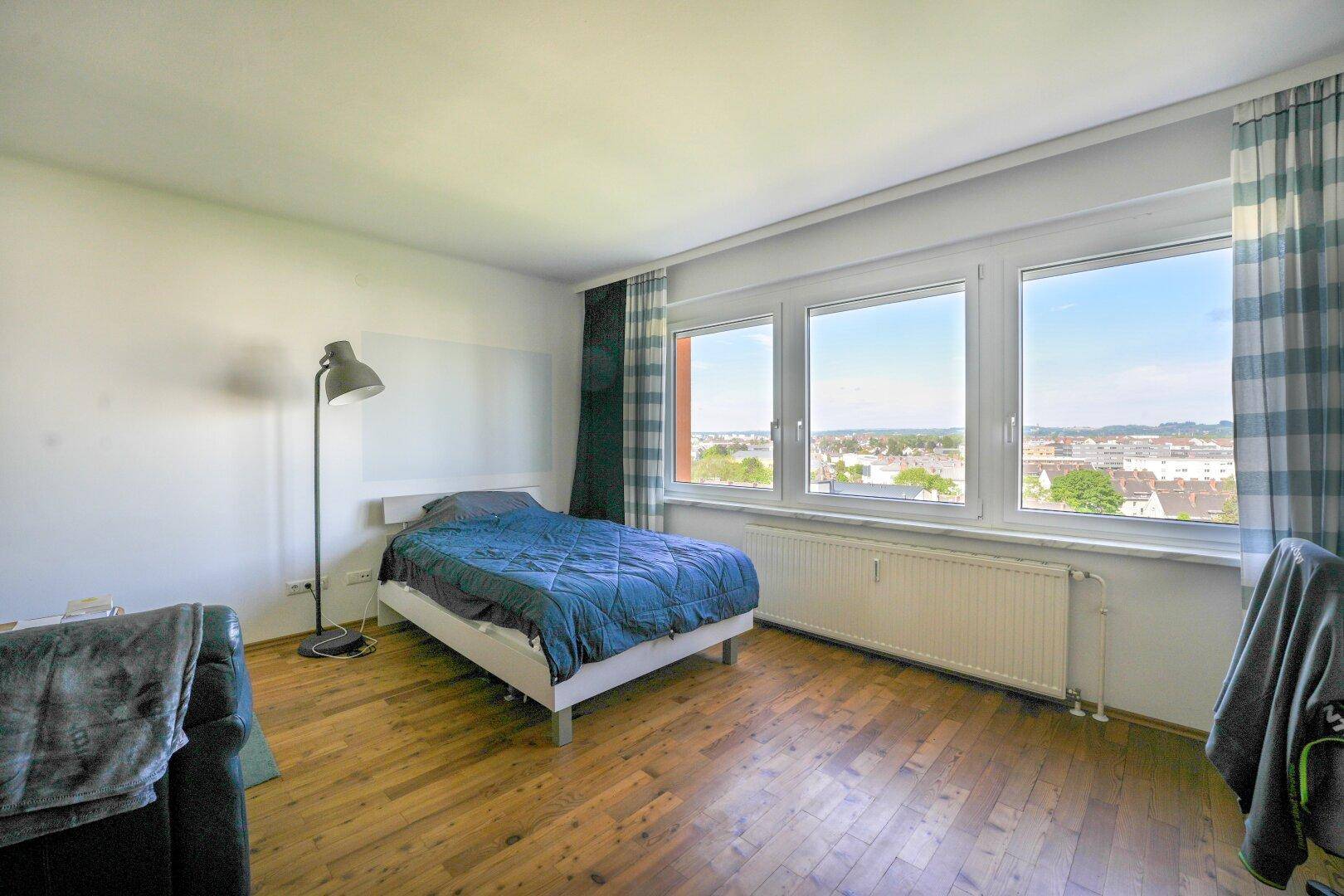 Geräumiges Schlafzimmer mit Doppelbett, Holzboden und großen Fenstern mit Stadtblick.