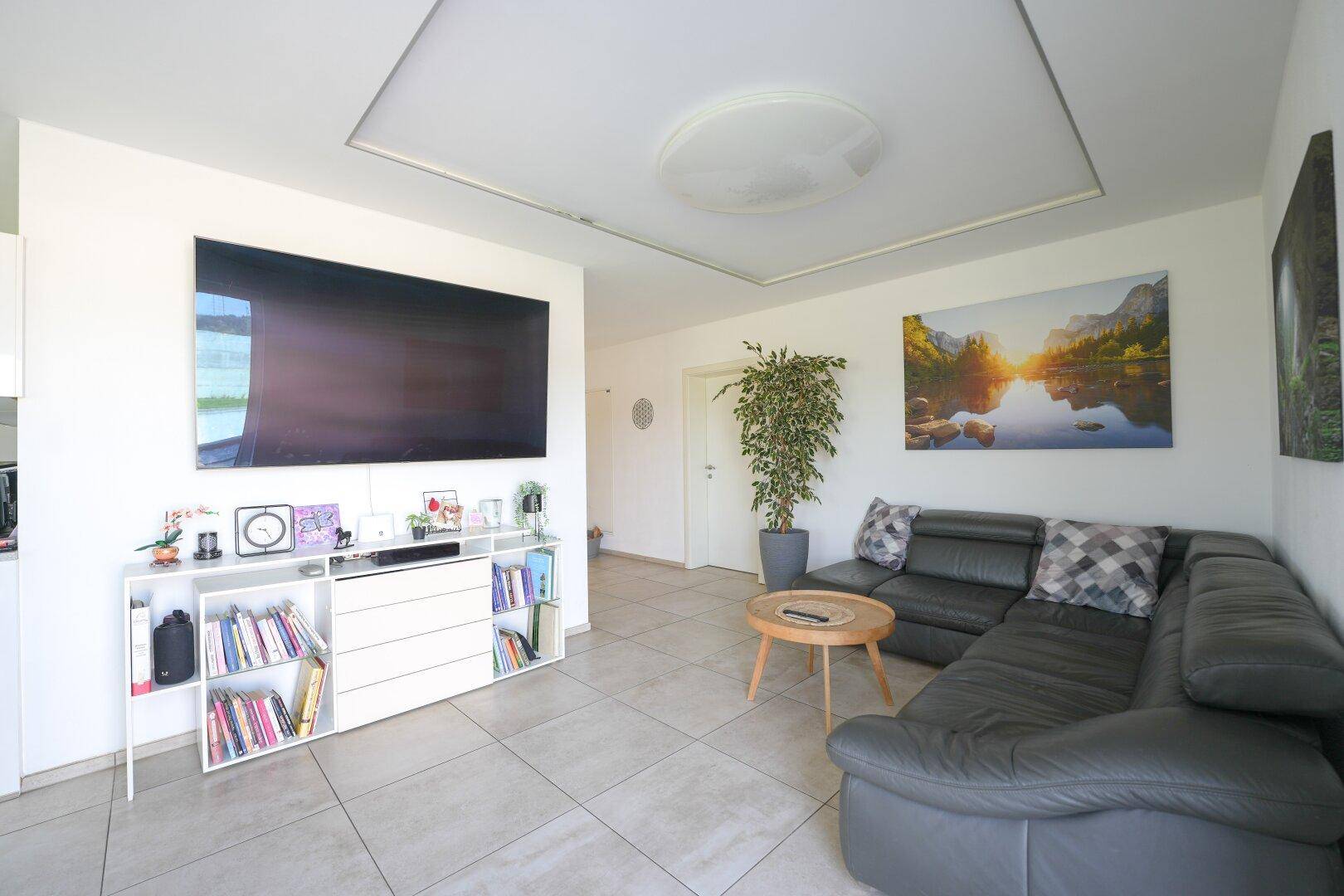 Modernes Wohnzimmer mit großem Fernseher, bequemer Eckcouch und hellem Fliesenboden.