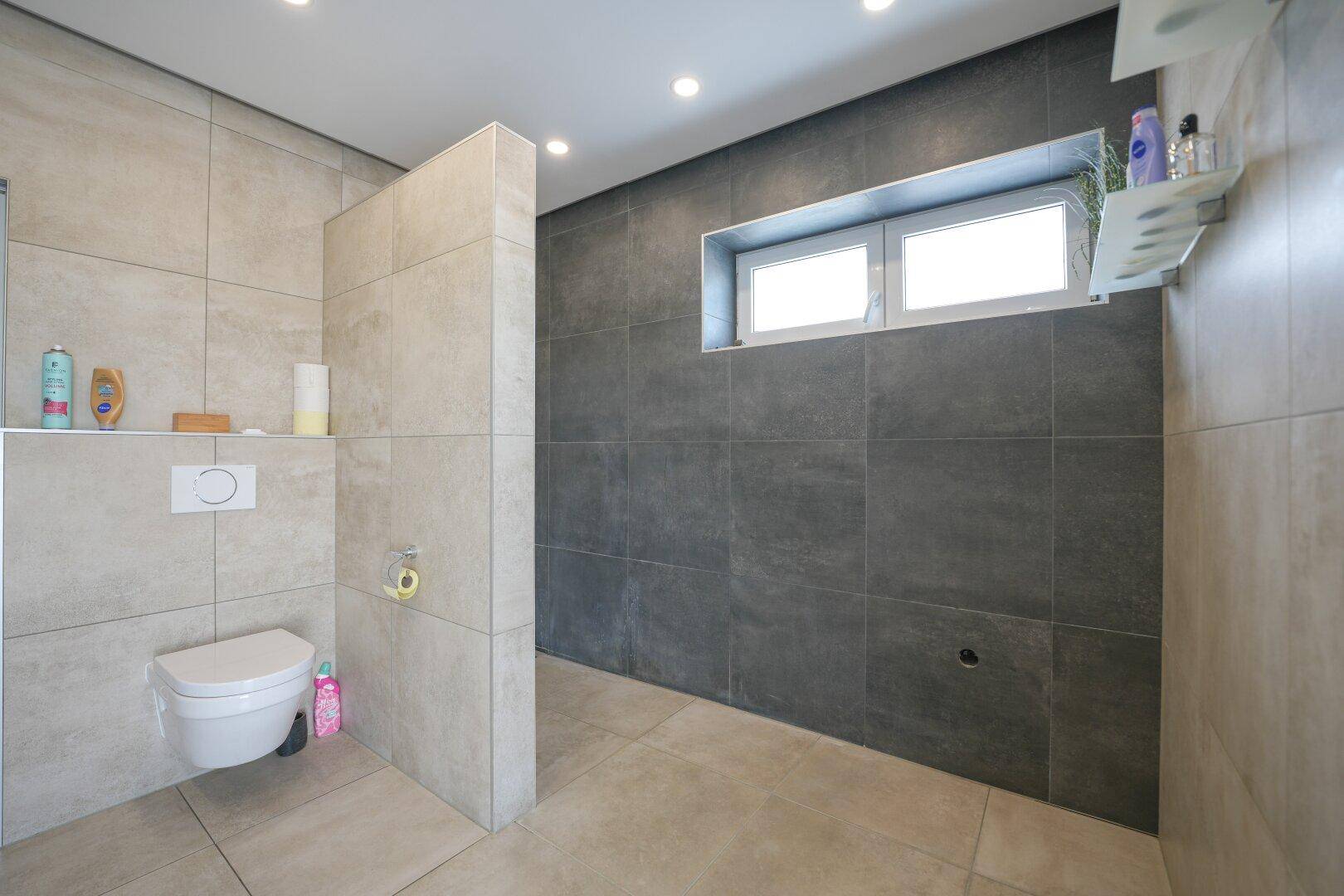 Modernes Badezimmer mit wandhängendem WC und einem kleinen Fenster für natürliche Belüftung.