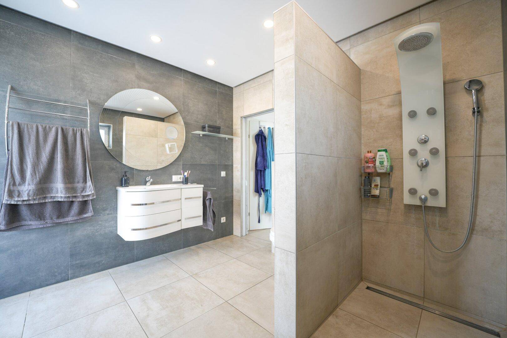 Modernes Badezimmer mit großformatigen Fliesen, schwebendem Waschtisch und geräumiger begehbarer Dusche.