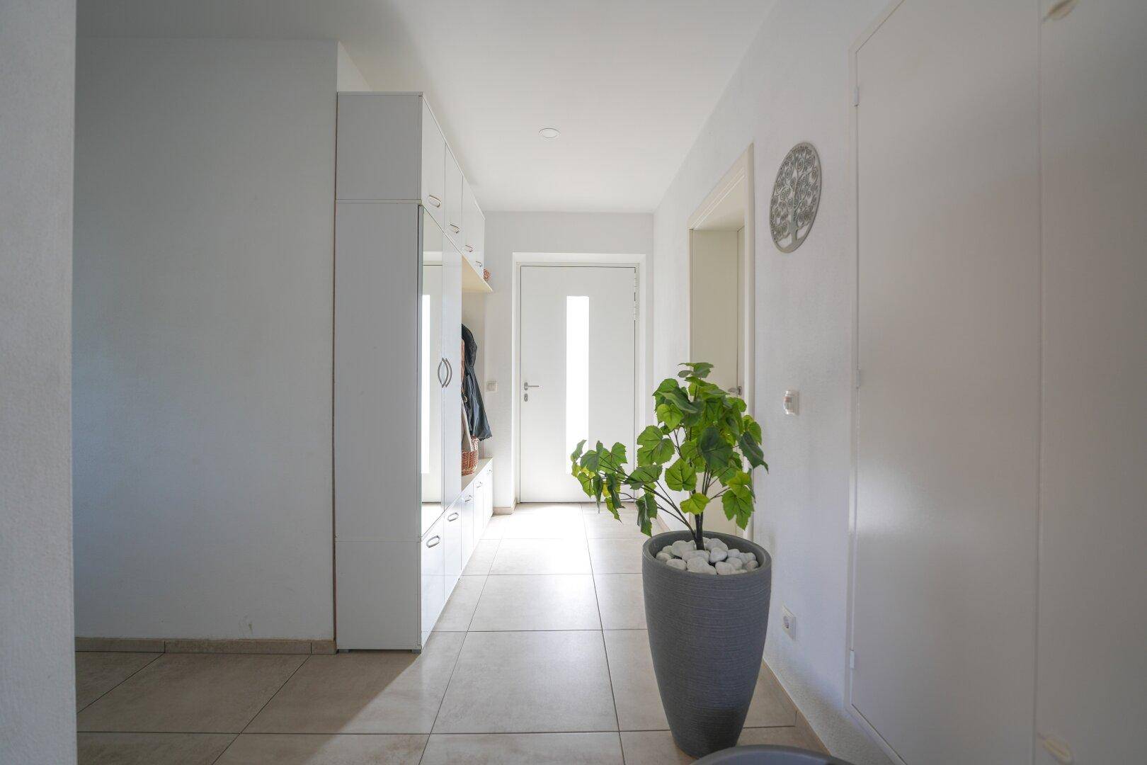 Heller Eingangsbereich mit modernen Fliesen, weißer Garderobe und einer dekorativen Pflanze.