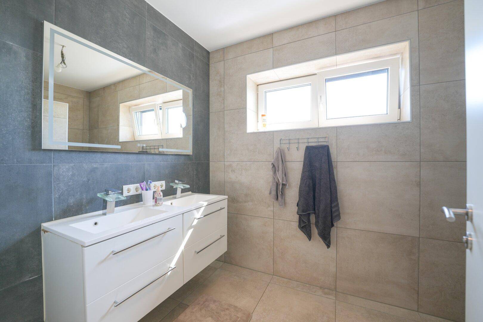Modernes Badezimmer mit Doppelwaschbecken, großem Spiegel und einem Fenster für Tageslicht.