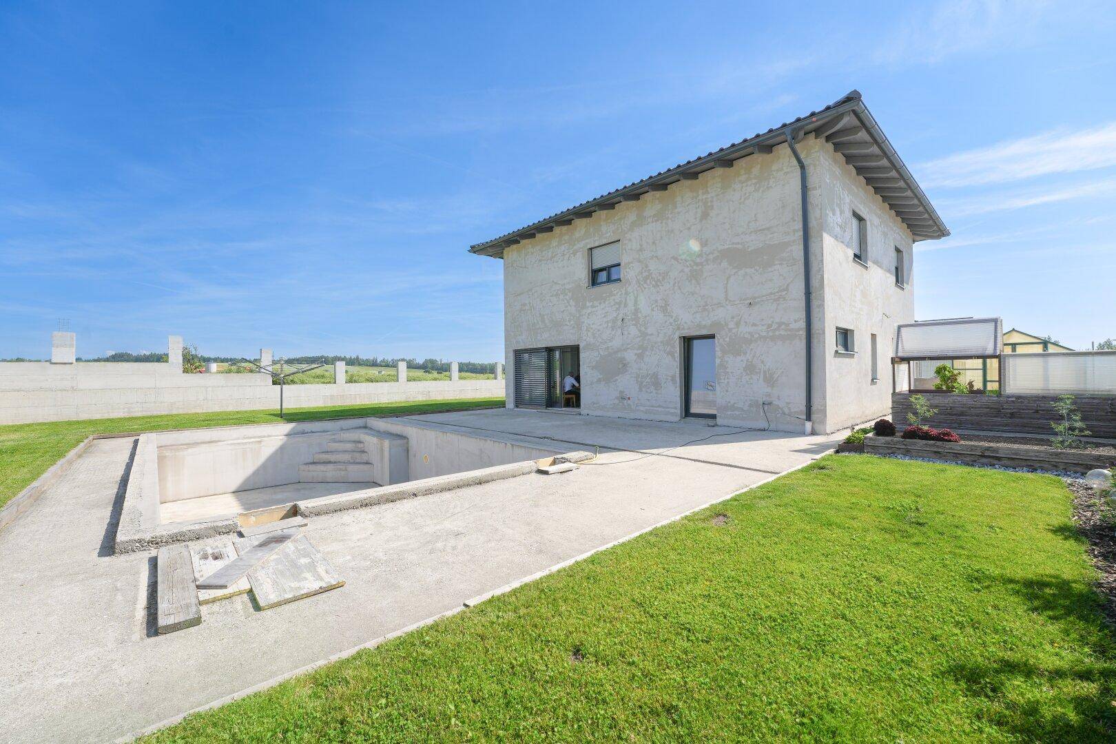 Neubau-Einfamilienhaus mit Rohbau-Pool und weitläufigem Garten in ländlicher Umgebung.