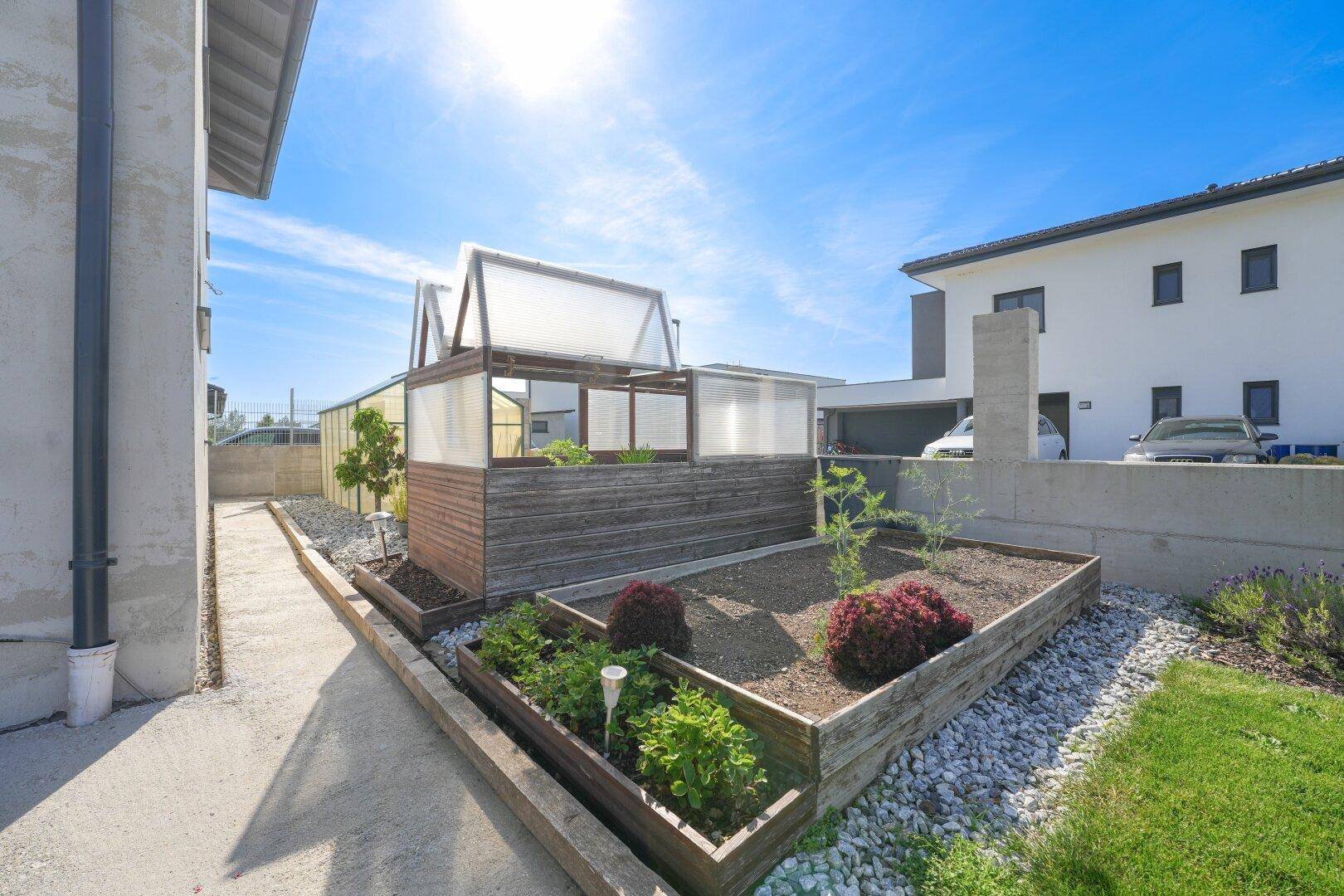 Angelegter Gartenbereich mit Hochbeeten, Kieswegen und verschiedenen Zierpflanzen.
