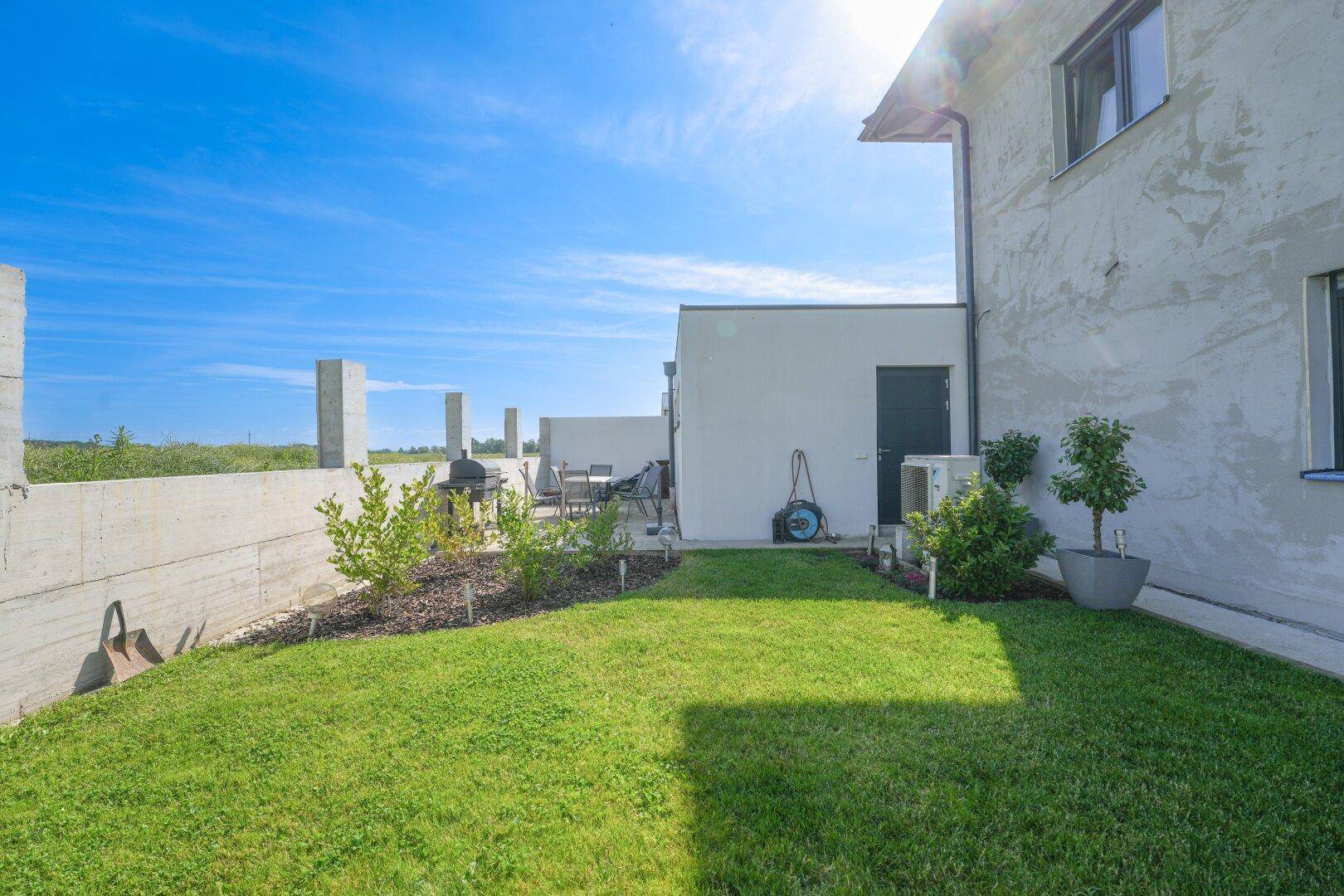Seitlicher Gartenbereich mit Rasen, einer gepflasterten Terrasse und Grillplatz.