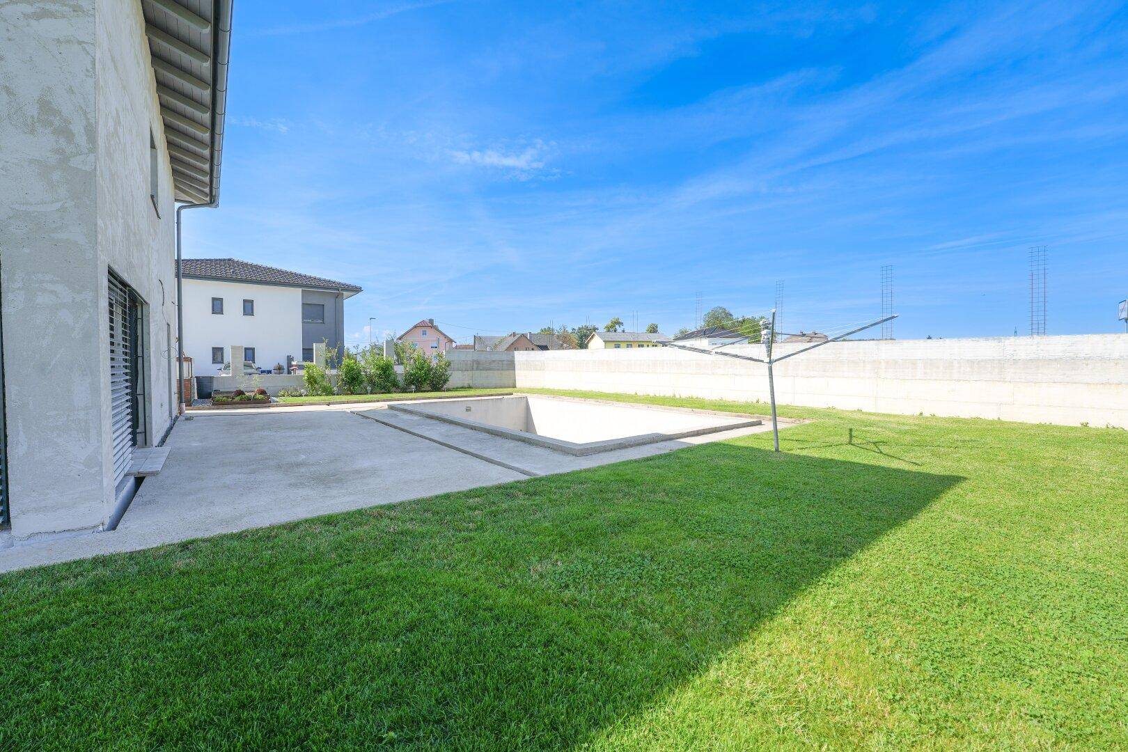 Weitläufiger Garten mit Rasenfläche, einem im Bau befindlichen Pool und der Hausfassade.