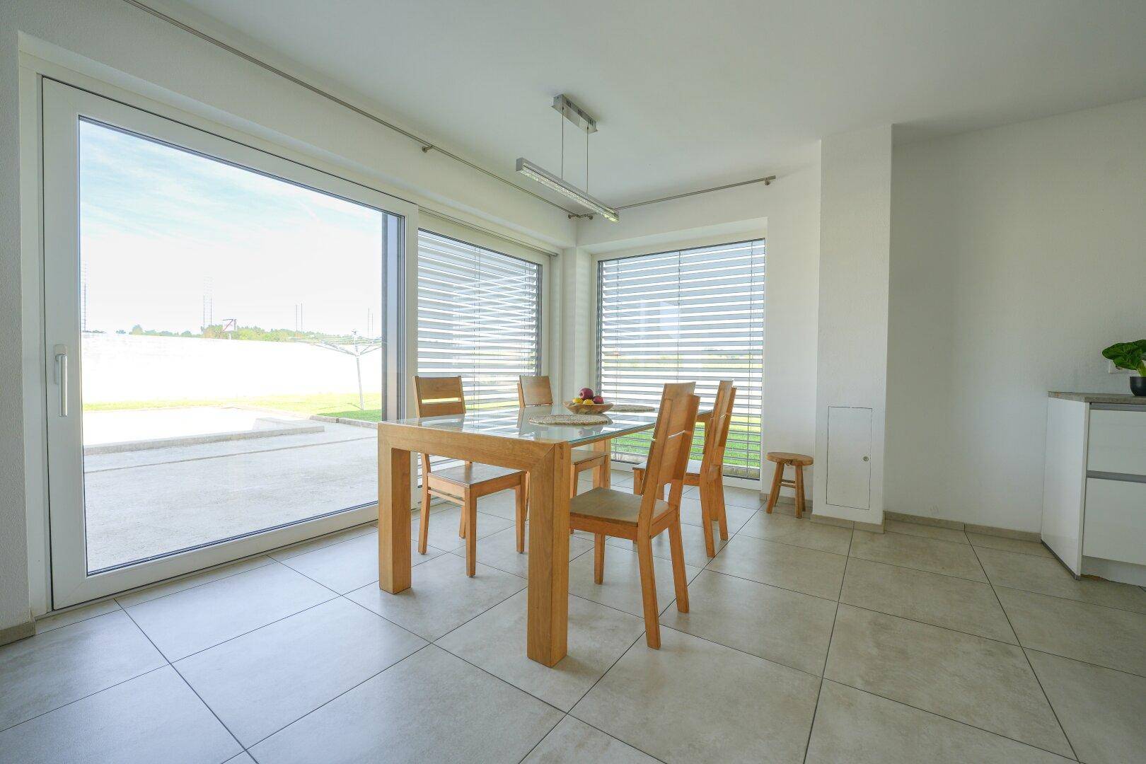 Heller Essbereich mit Holztisch, Stühlen und großen Fenstern mit Zugang zum Garten.