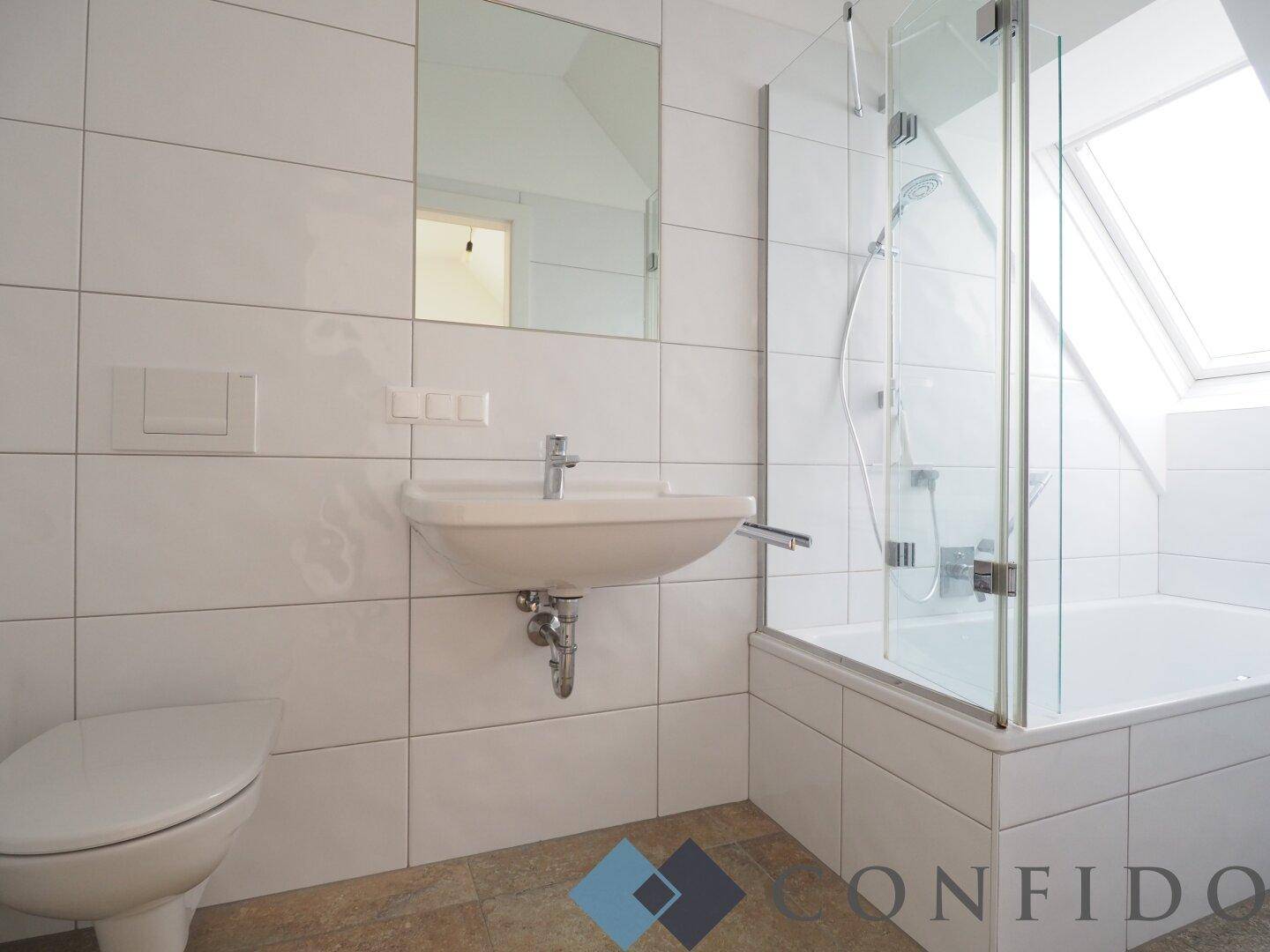 Helles Badezimmer mit weißen Fliesen, Badewanne mit Duschwand, WC und Waschbecken.