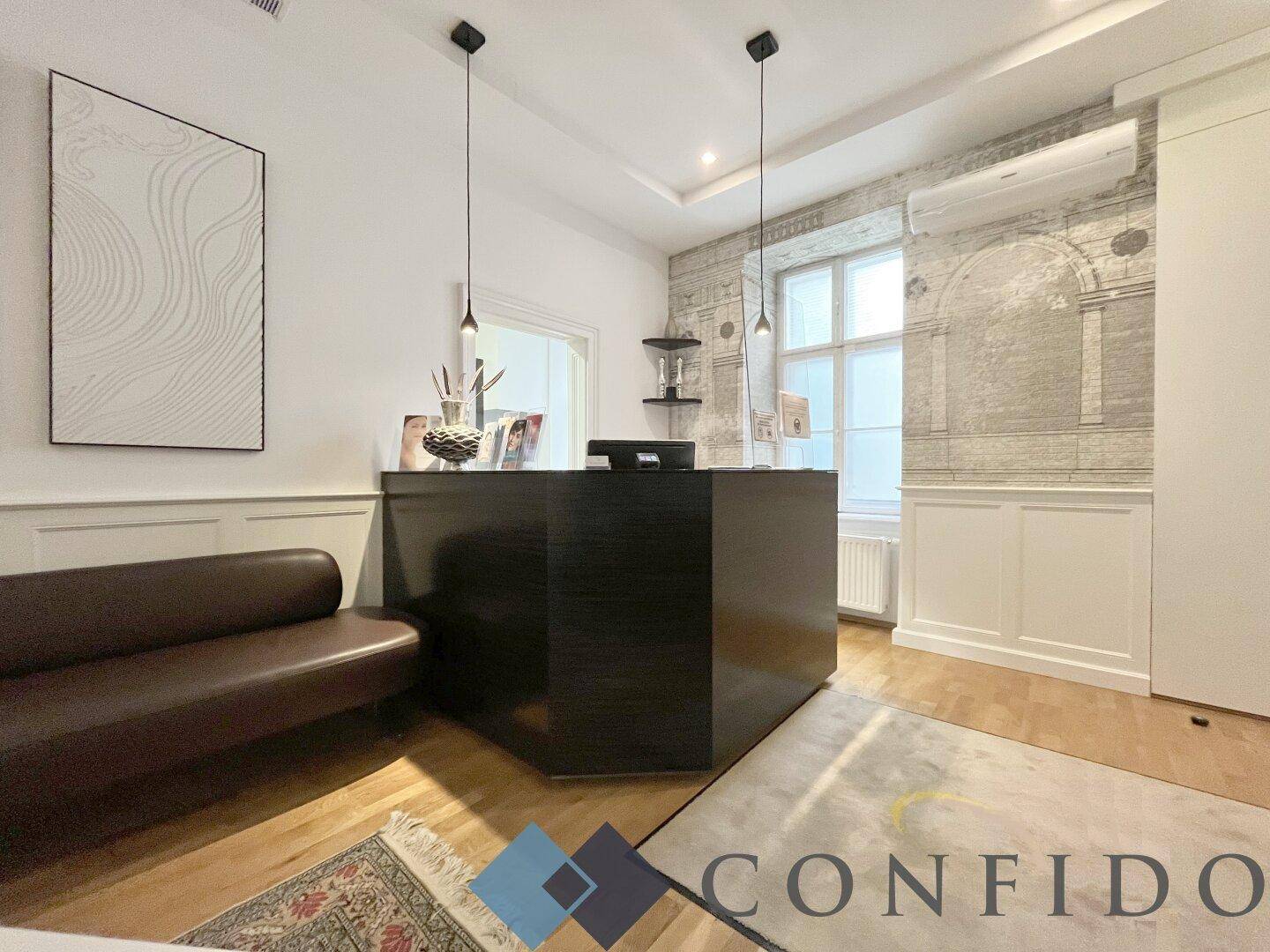 Detailansicht des Empfangsbereichs mit dunklem Tresen, braunem Sofa und einer dekorativen Wandgestaltung mit Fenster.