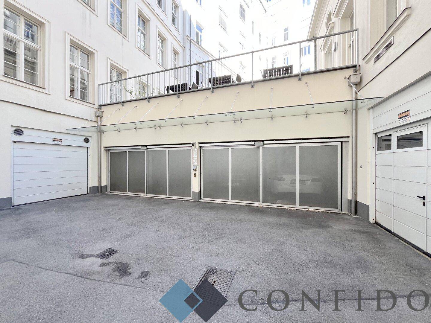 Innenhof mit Garagenzugängen und einer darüberliegenden Terrasse mit Geländer.
