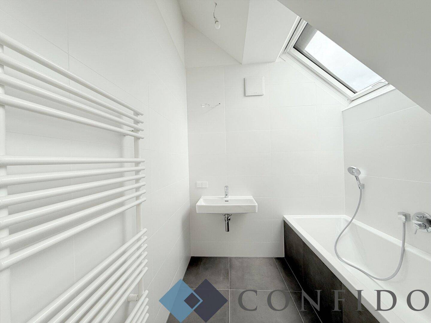 Modernes Badezimmer mit Badewanne, Einzelwaschbecken, Handtuchheizkörper und Dachfenster.