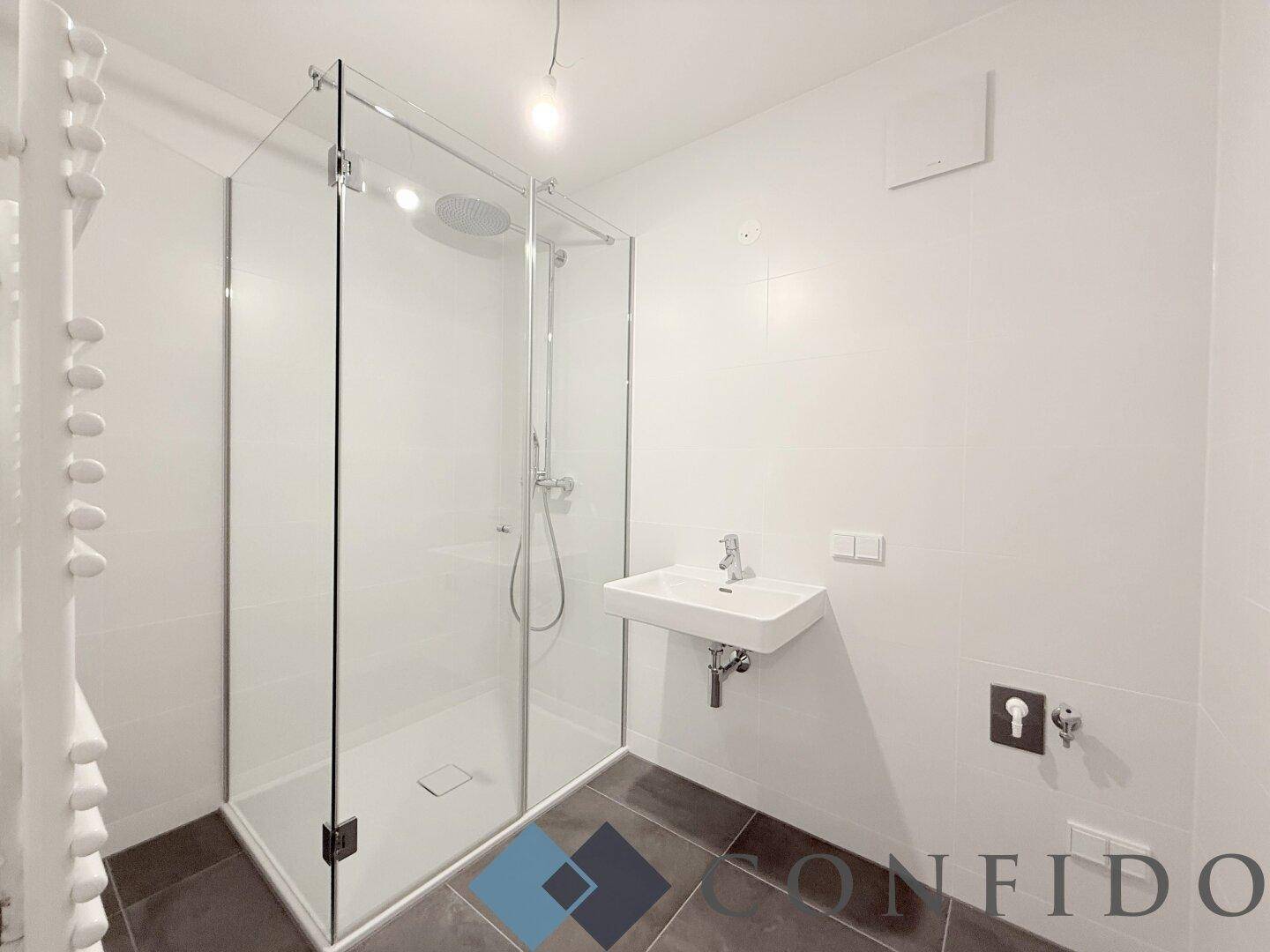 Modernes Badezimmer mit großer Glasdusche, Einzelwaschbecken und dunklen Bodenfliesen.