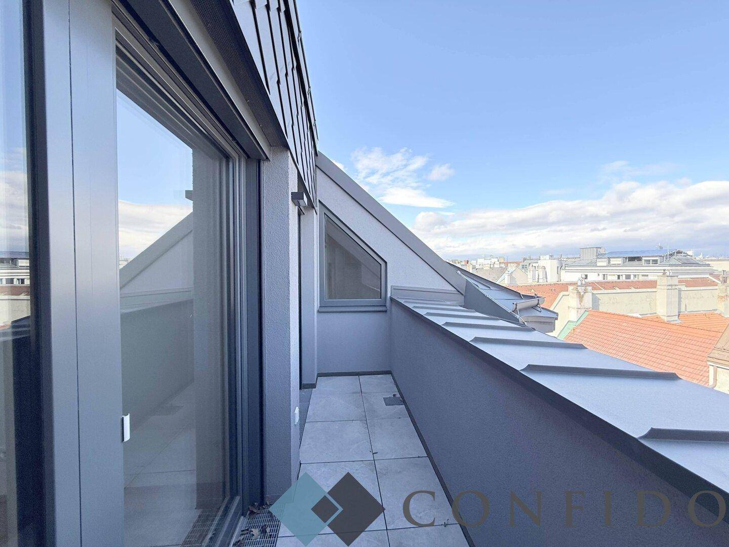 Kleiner Balkon mit Fliesenboden und Blick auf die umliegenden Dächer der Stadt.