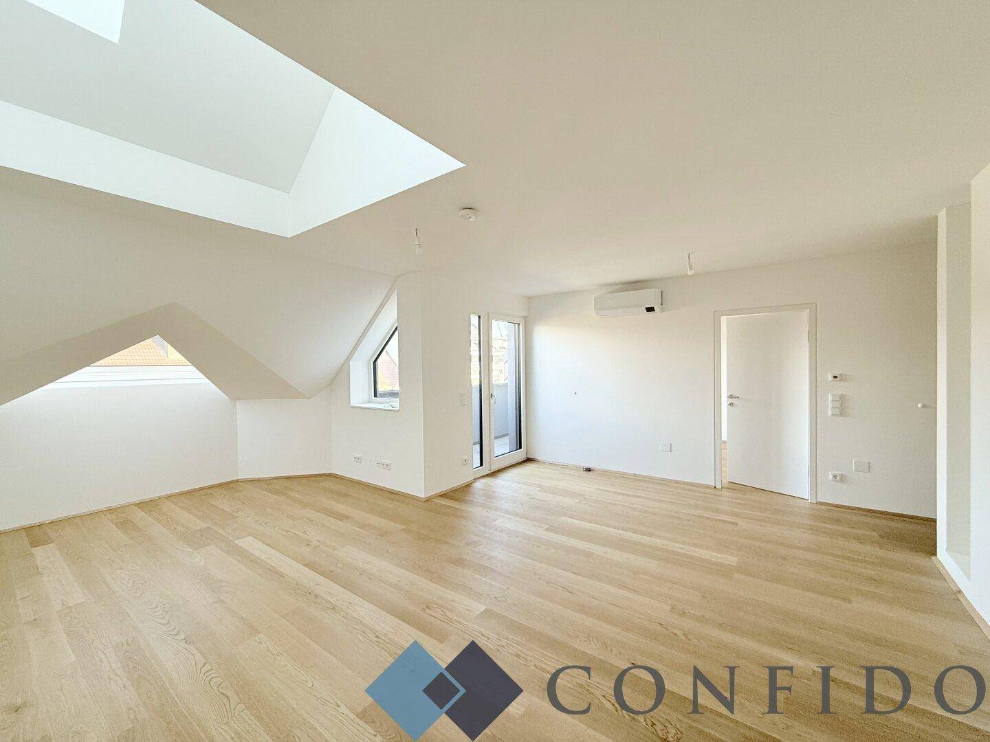 Heller Wohnraum im Dachgeschoss mit Holzboden, Dachfenstern und Zugang zu einem Balkon.
