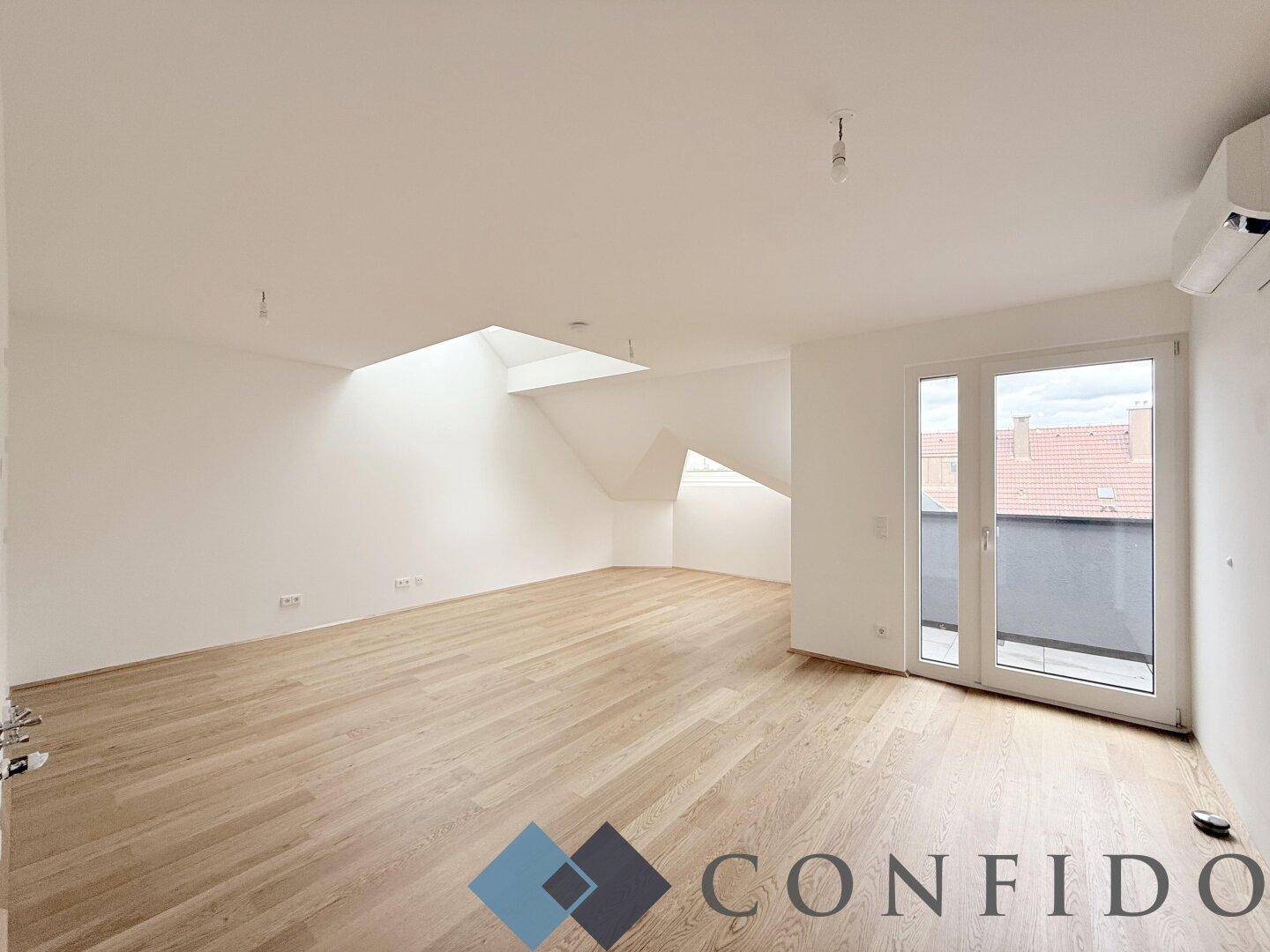 Lichtdurchfluteter Dachgeschossraum mit Holzboden, Klimaanlage und Zugang zu einem kleinen Balkon.